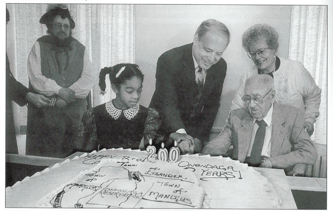 Aisha Mitchell, county executive Nick Pirro, and centenarian Ed Sauer cut a birthday cake in the shape of Onondaga County during the bicentennial celebration at OHA in 1994.